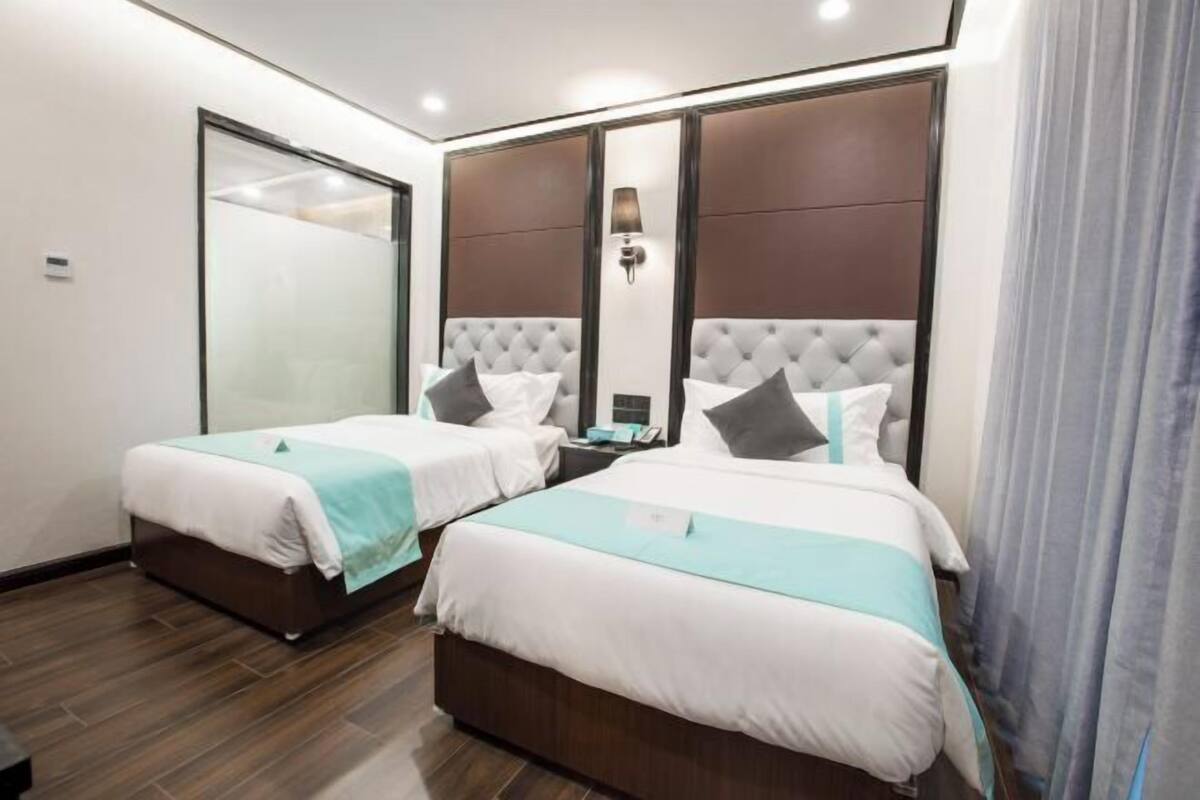 A hotel room with two beds, a large mirror, a nightstand, and a window with curtains.
