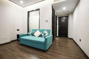A modern hotel room with a teal sofa, wooden flooring, and a large mirror. - Xi . Hotel (Huidong)