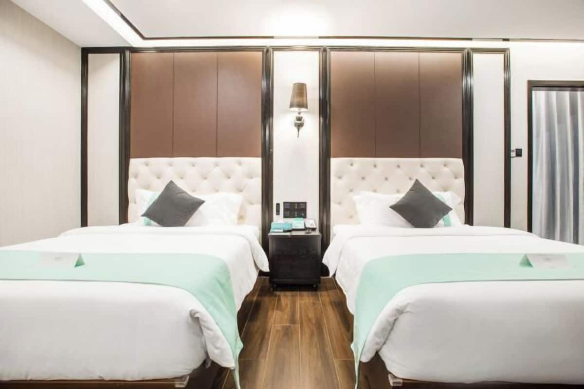A hotel room with two beds, a nightstand, a lamp, and a wardrobe.