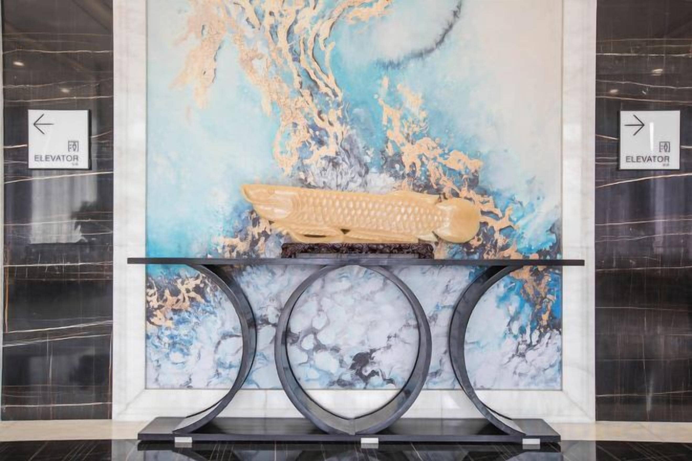A reception area with a marble wall, a central console with a keyboard, and directional signs for the elevator.