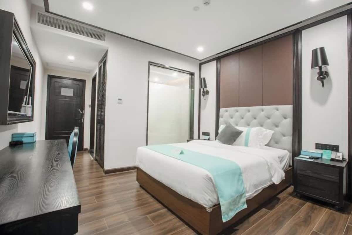 A modern hotel room with a large bed, a desk, a wardrobe, and a mirror.
