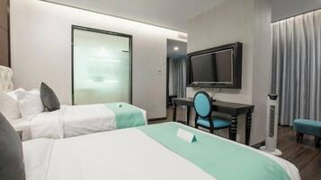 Quarto de hotel com duas camas, uma escrivaninha com cadeira, televisão e janela com cortinas.