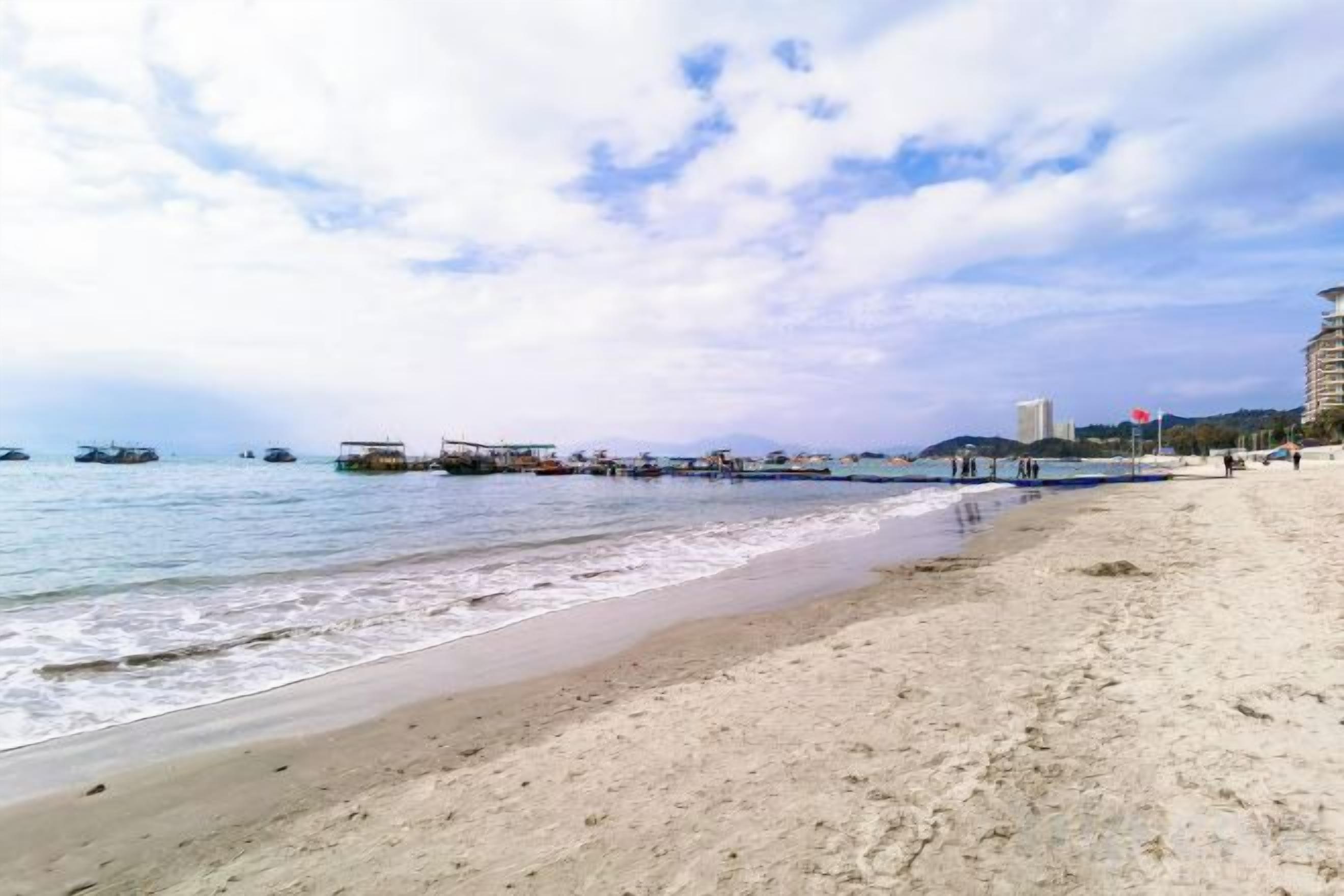 A beach with a sandy shore, calm water, and a pier extending into the sea.