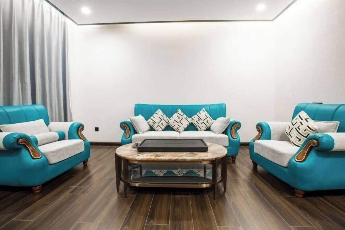 A modern living room with teal sofas, a central coffee table, and patterned cushions.