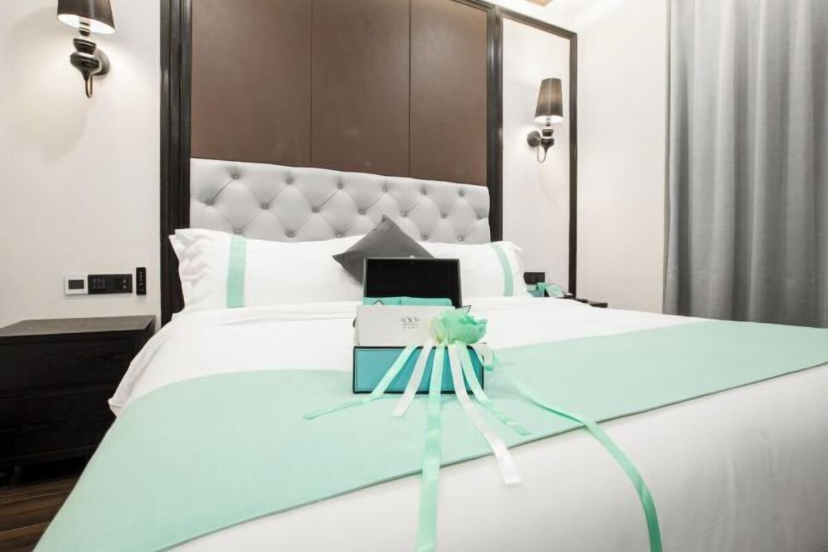 A hotel room with a large bed, a tufted headboard, and a teal bedspread.