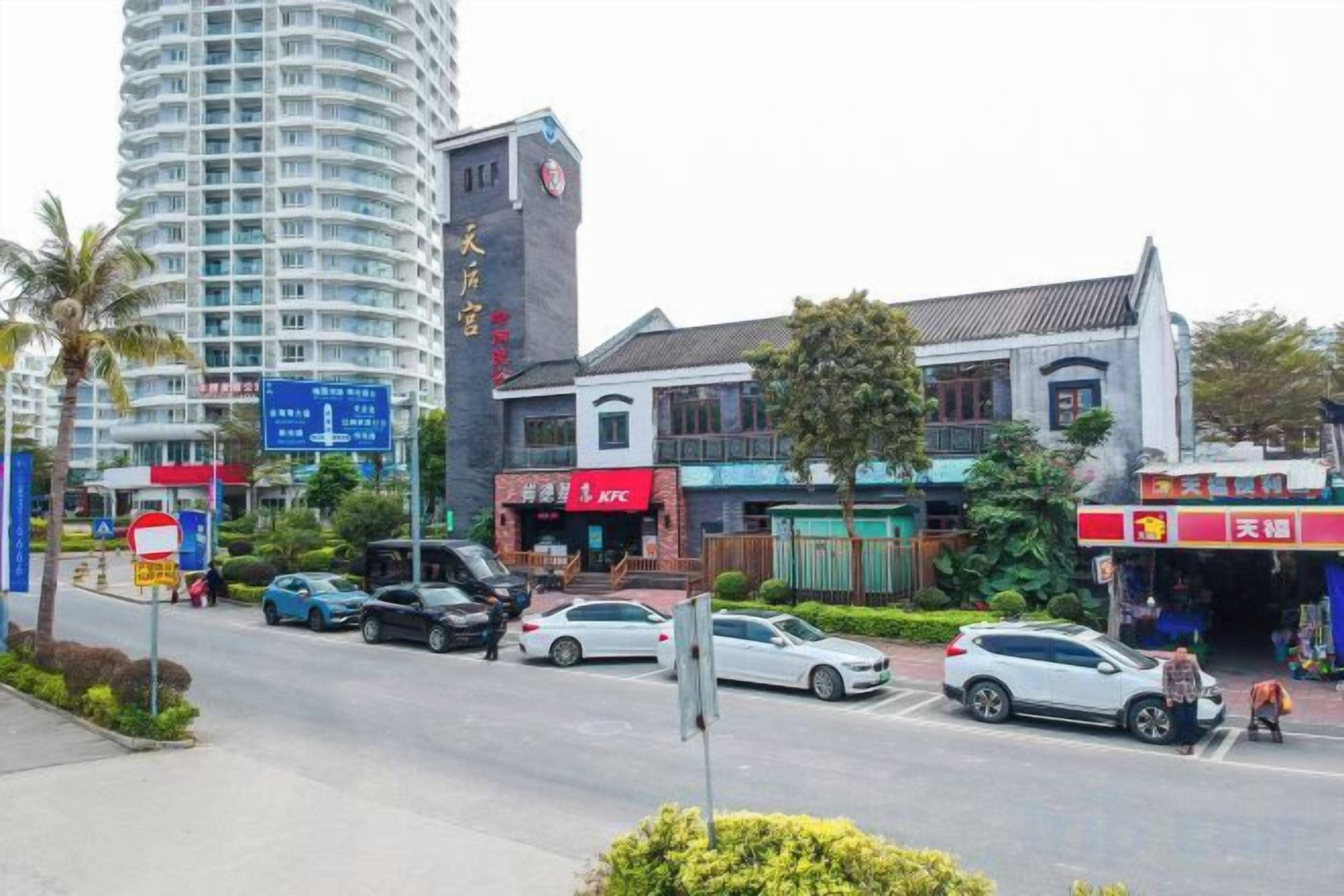 Vista de la calle con un edificio residencial alto, un restaurante KFC y una tienda de conveniencia.