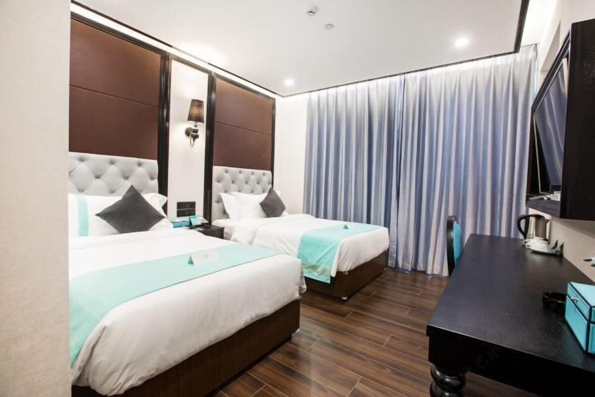 A hotel room with two beds, a desk, and a large window with curtains.