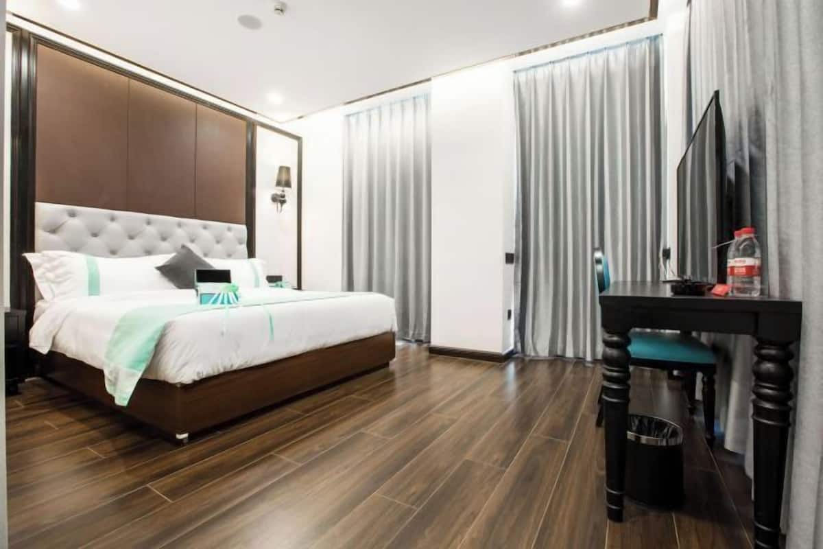 A bedroom with a large bed, a desk, a TV, and a trash bin.