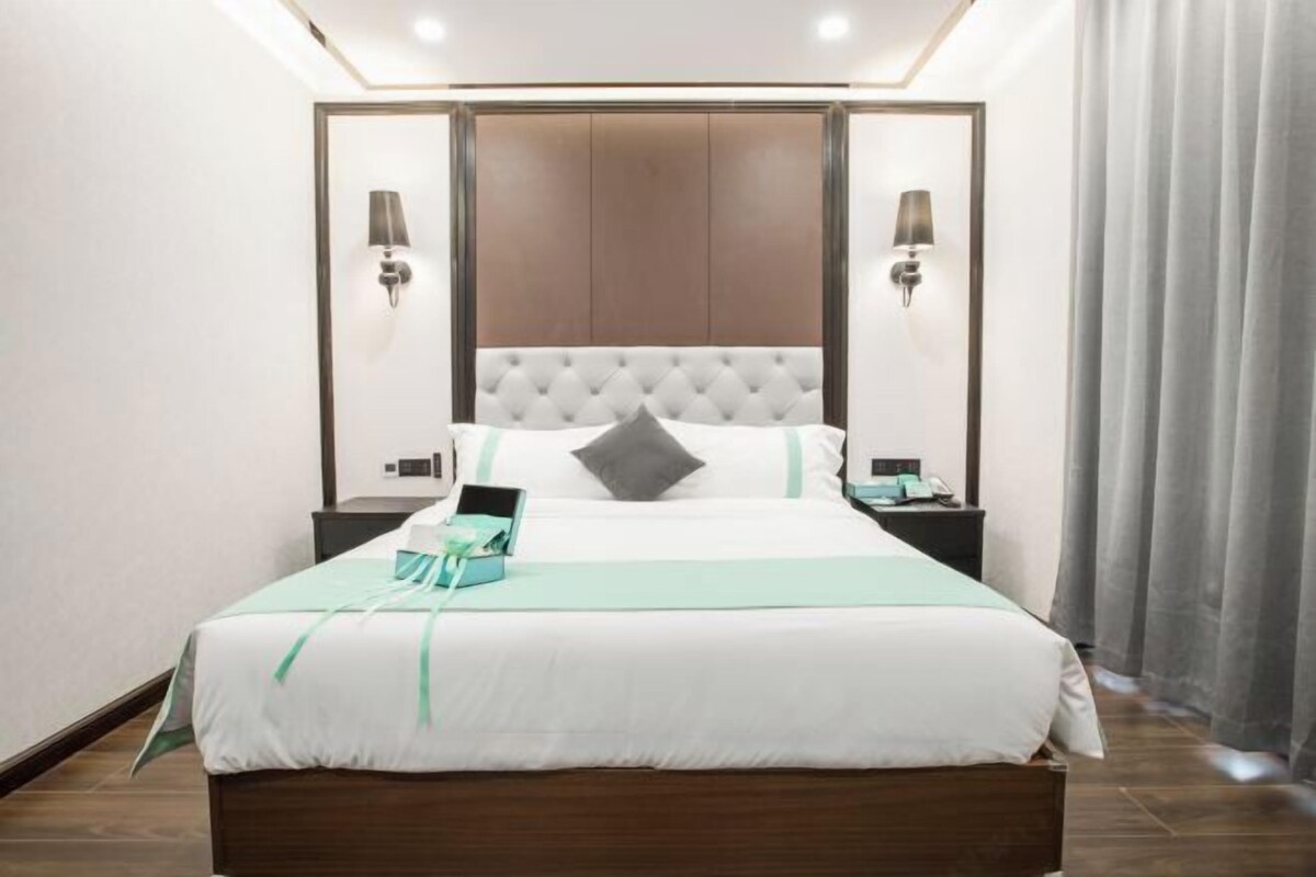 A neatly made bed with a white and green bedspread, a grey pillow, and a bedside table with a lamp.