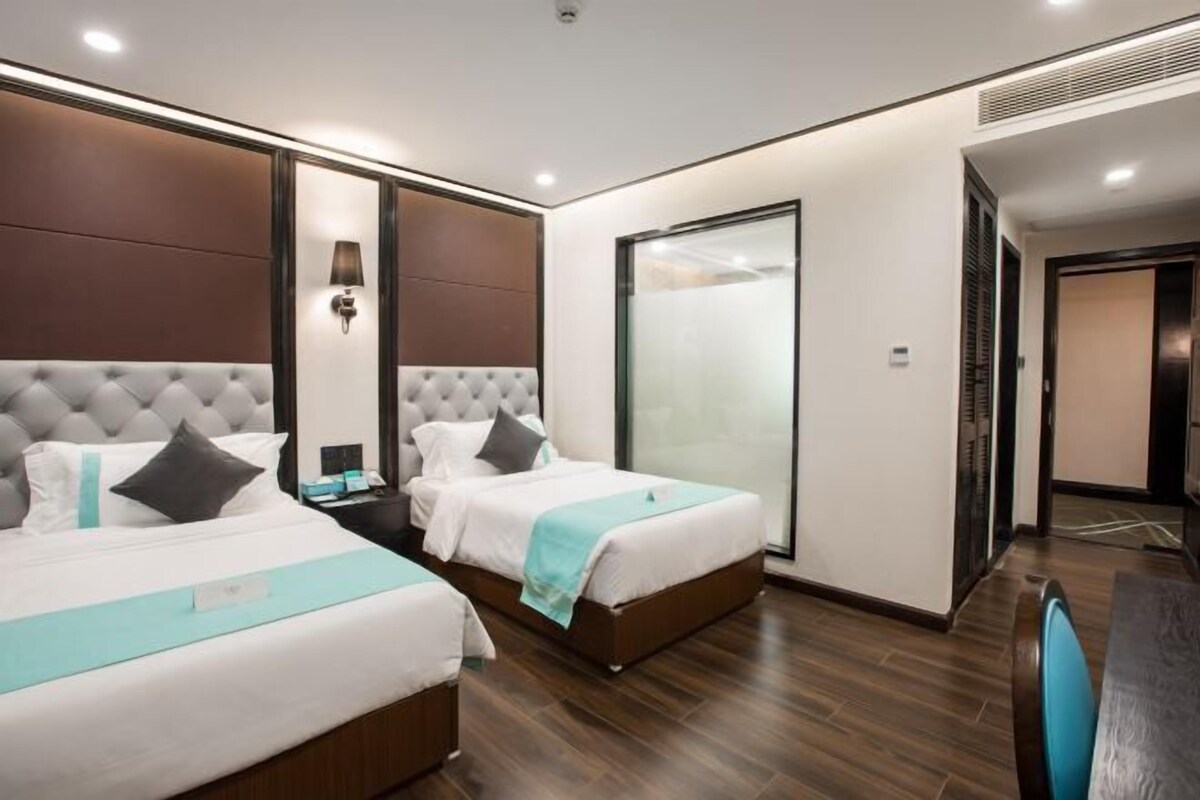 A hotel room with two beds, a desk, and a large window.