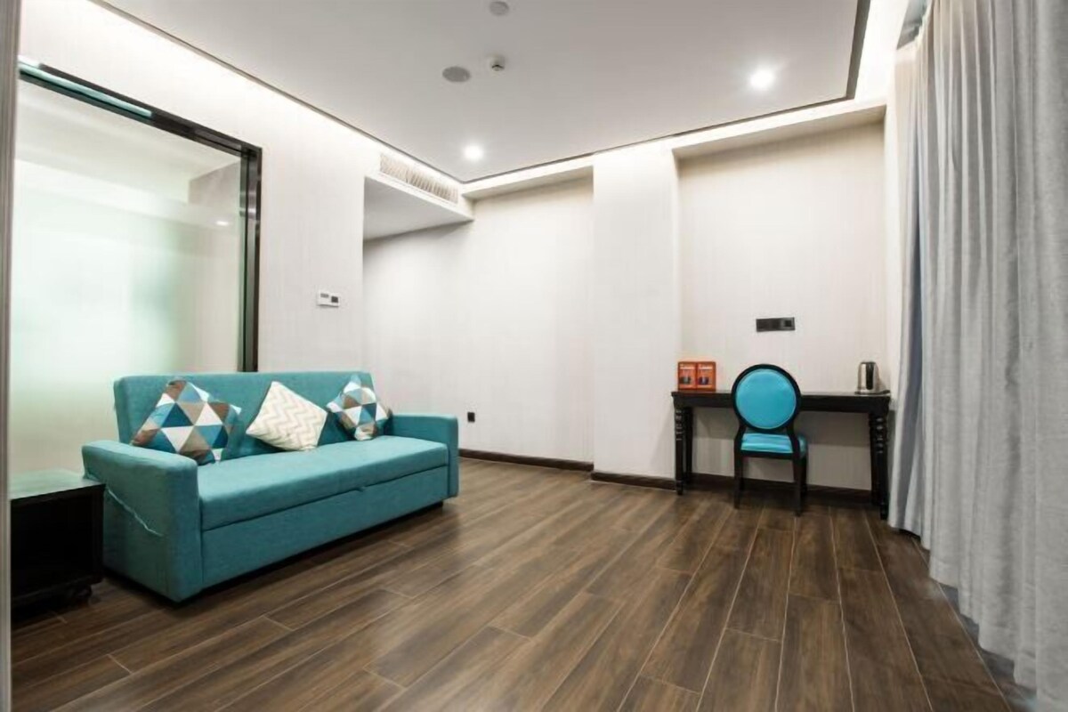 A modern living room with a teal sofa, a wooden floor, and a desk with a chair.