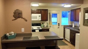 A compact kitchen with a central island, dark wooden cabinets, and a white stove. - Bootlegger Bungalow - Downtown Anchorage (Anchorage)