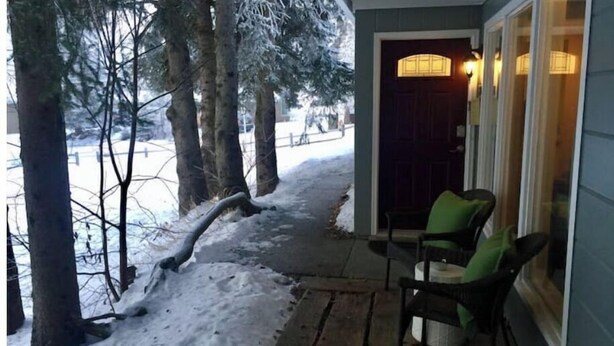 A covered porch with a wooden bench and chairs, a snow-covered path, and a door leading to a building. - Bootlegger Bungalow - Downtown Anchorage (Anchorage)