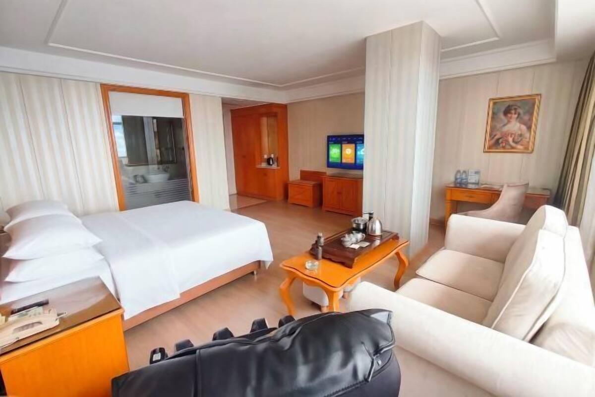 Habitación de hotel con cama, sofá, televisión, mesa de centro y baño visible a través de una puerta.
