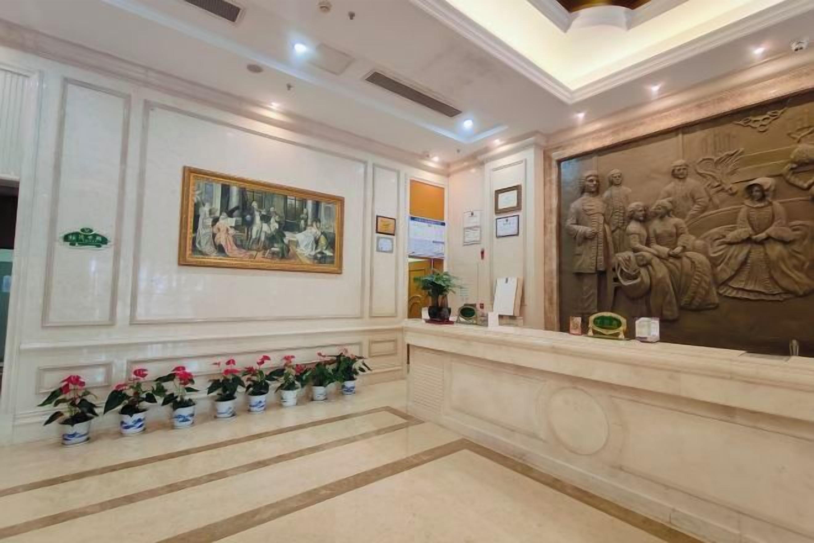 A reception area with a marble floor, a reception desk, a framed painting, and a relief sculpture.