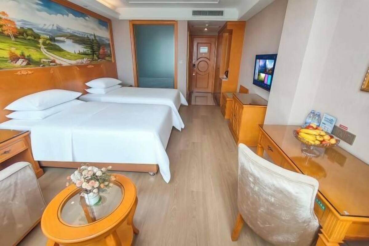 Habitación de hotel con dos camas, un escritorio, un televisor y un cuadro en la pared.