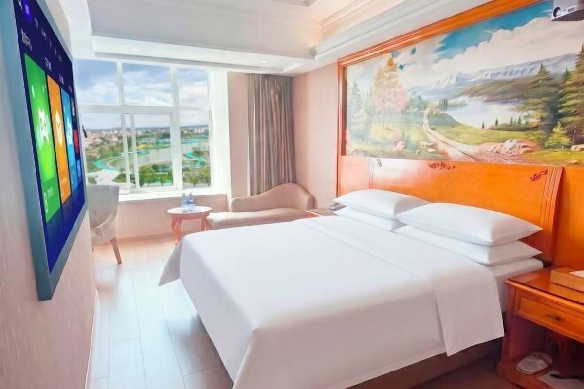 Habitación de hotel con una cama grande, un escritorio, una silla, una mesita y un cuadro en la pared.