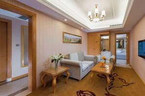 A hotel room with a sofa, a small table with flowers, a television, and a hallway leading to another room. - Vienna Hotel (Taihe Chengjiang Avenue) (Taihe)