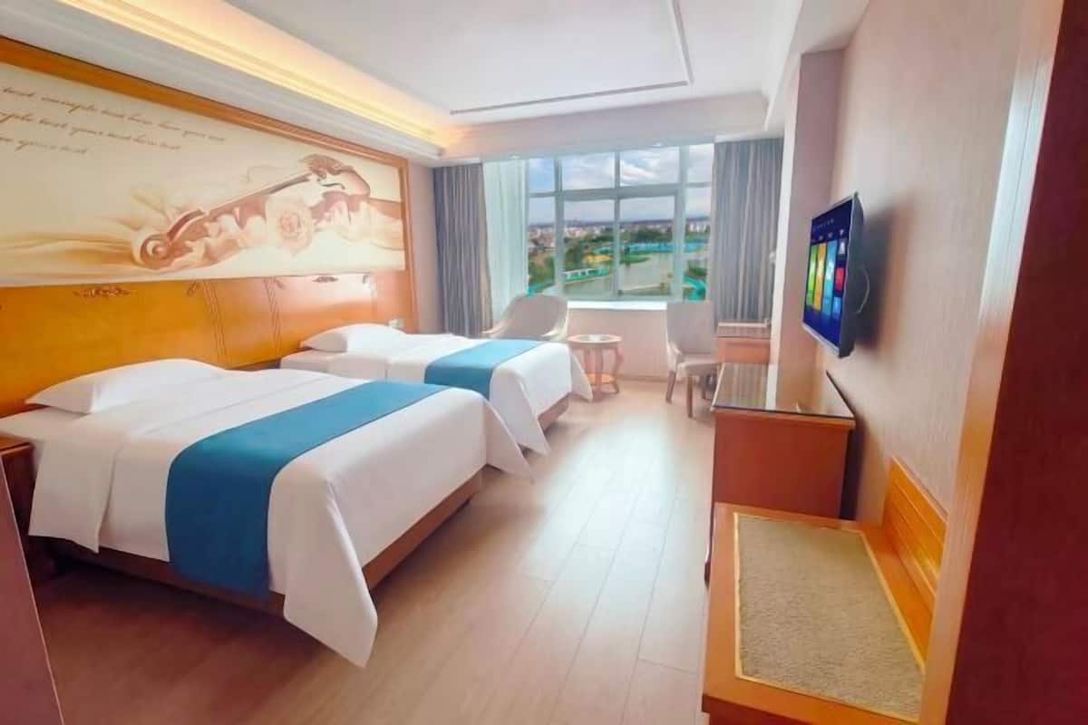 Habitación de hotel con dos camas, un escritorio, una silla, un televisor y una ventana con vistas.