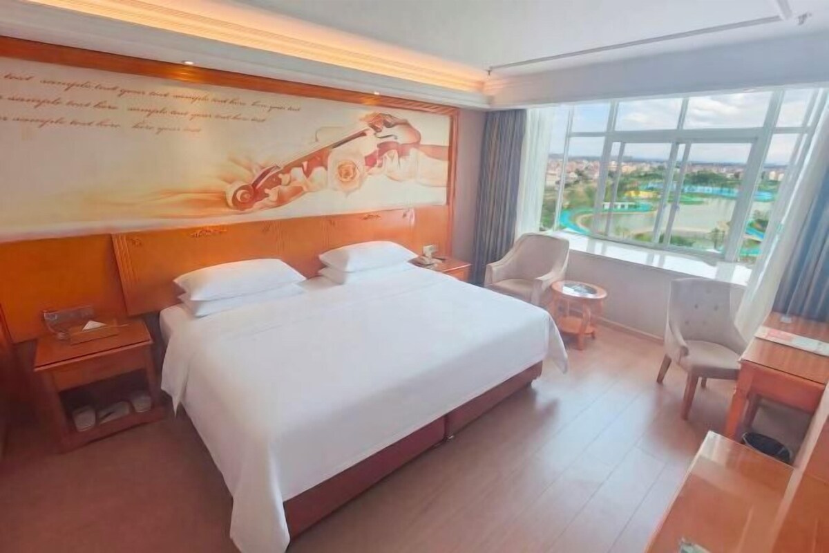 A hotel room with a large bed, a desk, a chair, and a view of a body of water.