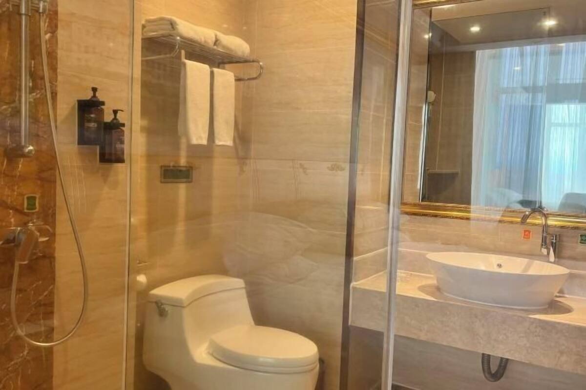 Un baño con ducha envuelta en vidrio, inodoro, lavamanos con espejo y perchero para toallas.