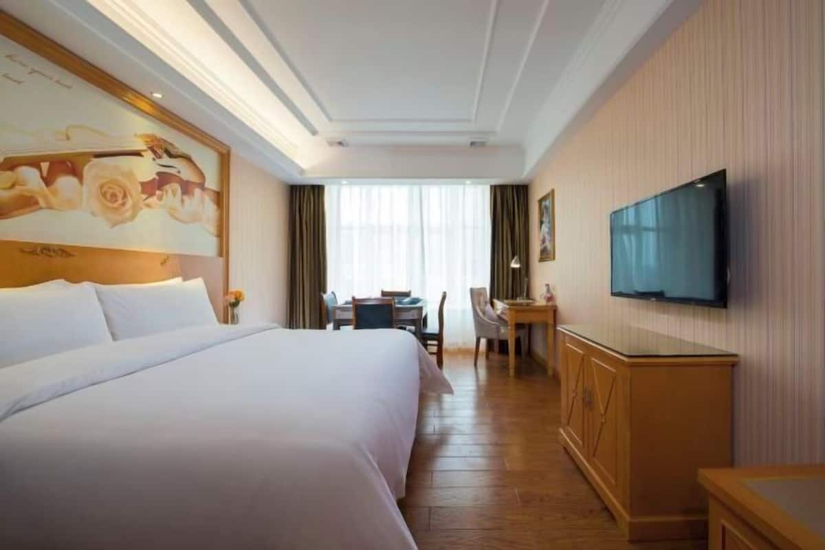 Un cuarto de hotel con una cama grande, un escritorio, una silla, un televisor y un cuadro en la pared.