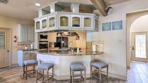 Una cucina con isola centrale, sgabelli da bar, microonde, forno e lavello.
