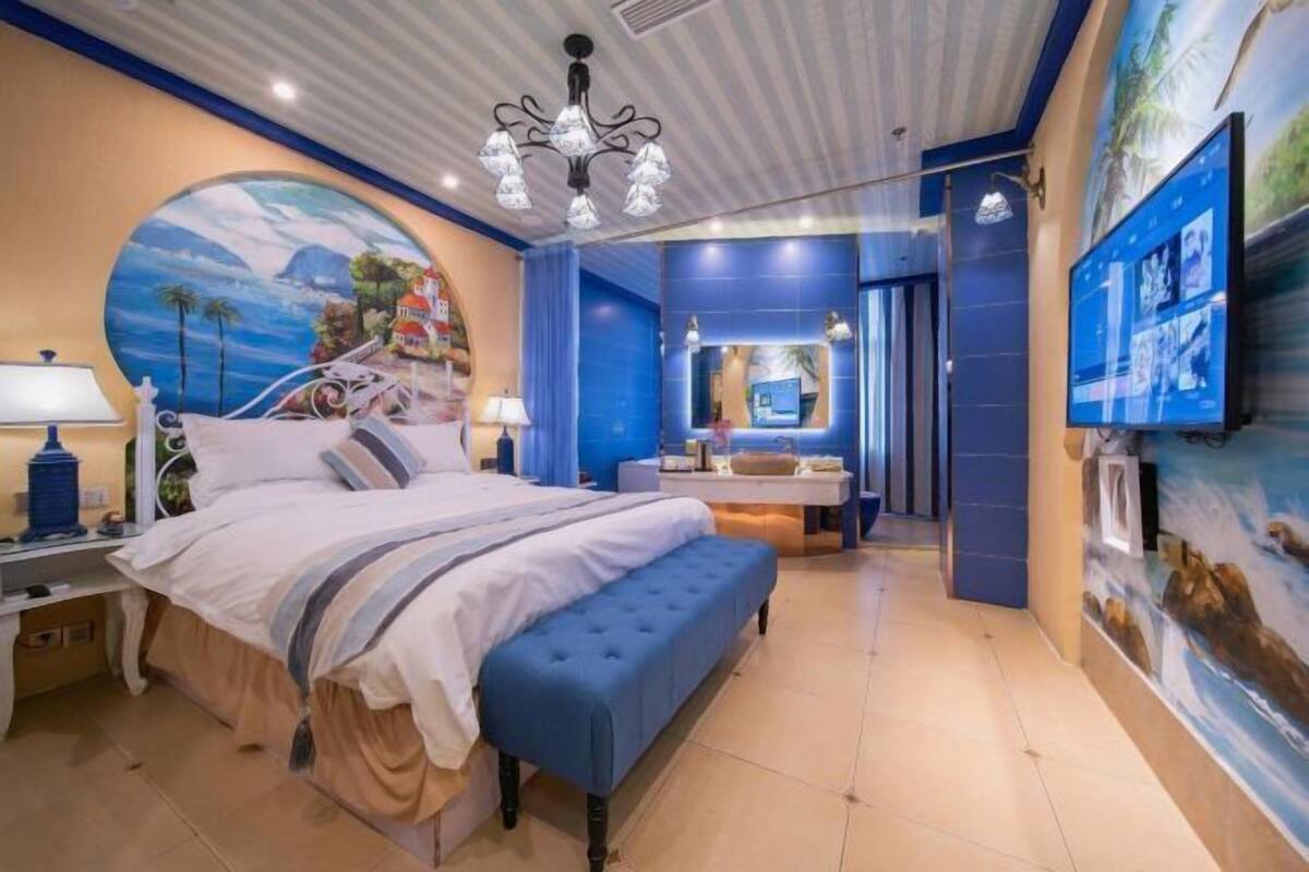 A bedroom with a large bed, a bench, a desk, and a TV.