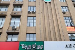 A multi-story building with air conditioning units on the exterior, a green sign with white text, and a red sign with white text. - Rugao Wonderland Midi Hotel (RT Mart Wuyue Plaza Store) (Rugao)