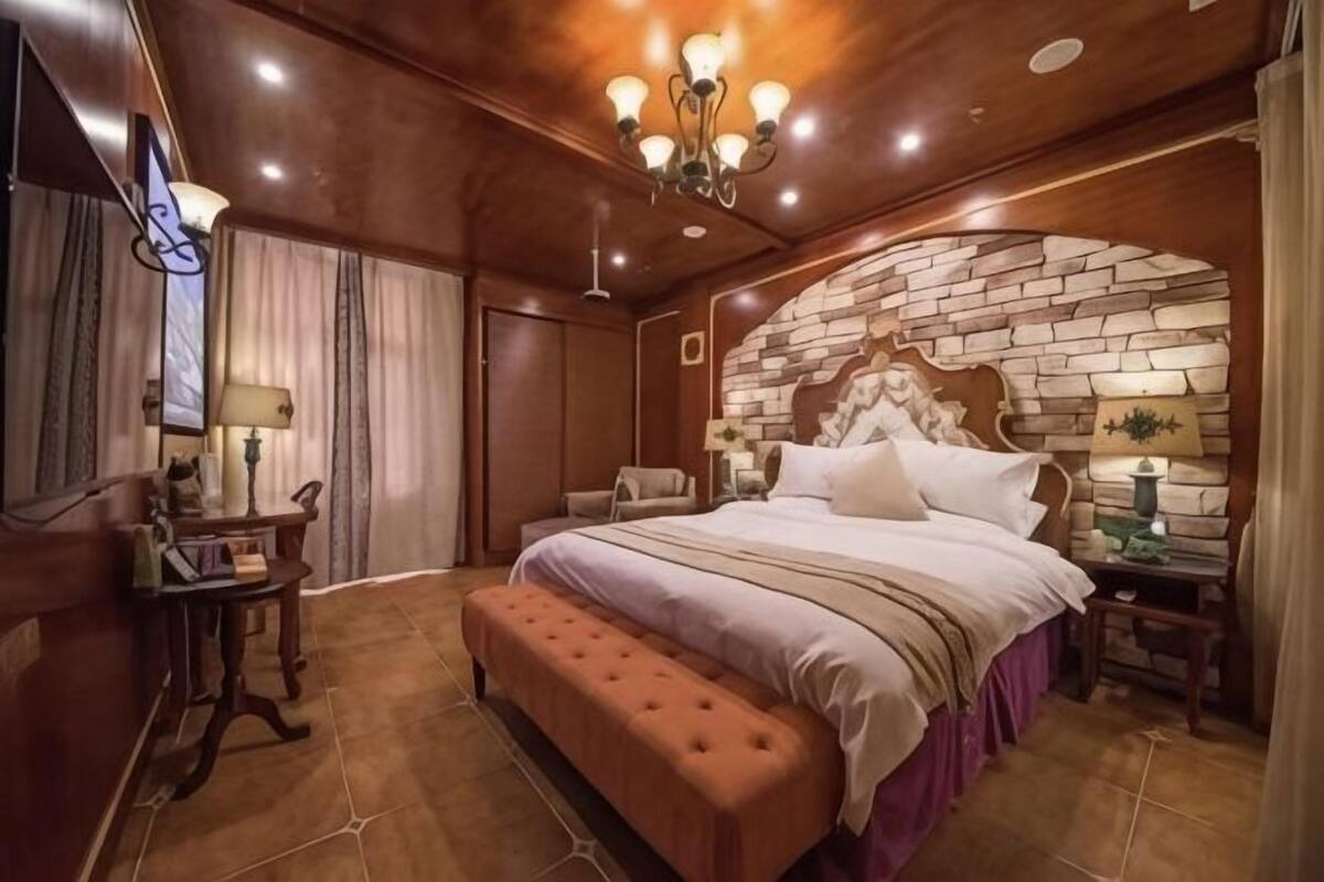 A bedroom with a large bed, a wooden headboard, a bench, a desk, and a chair.