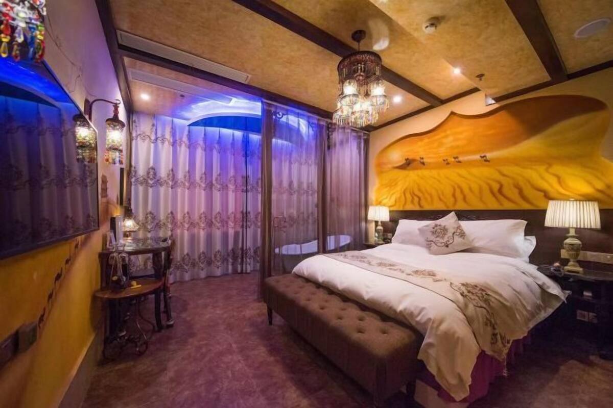 A bedroom with a large bed, a bench, a table, and a chandelier.