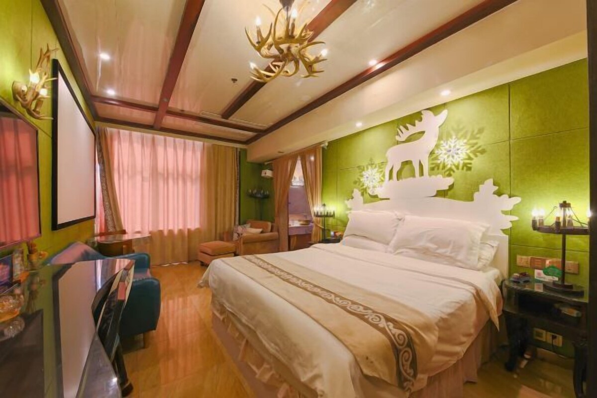 Une chambre d’hôtel avec un grand lit, un bureau avec une chaise, une télévision et un mur d’accent vert orné d’un motif représentant un cerf et des flocons de neige.