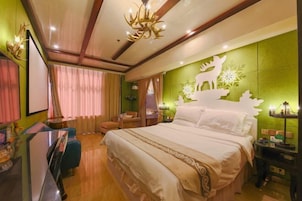 Habitación de hotel con una cama grande, un escritorio con silla, televisor y una pared verde decorada con un diseño de ciervo y copo de nieve.