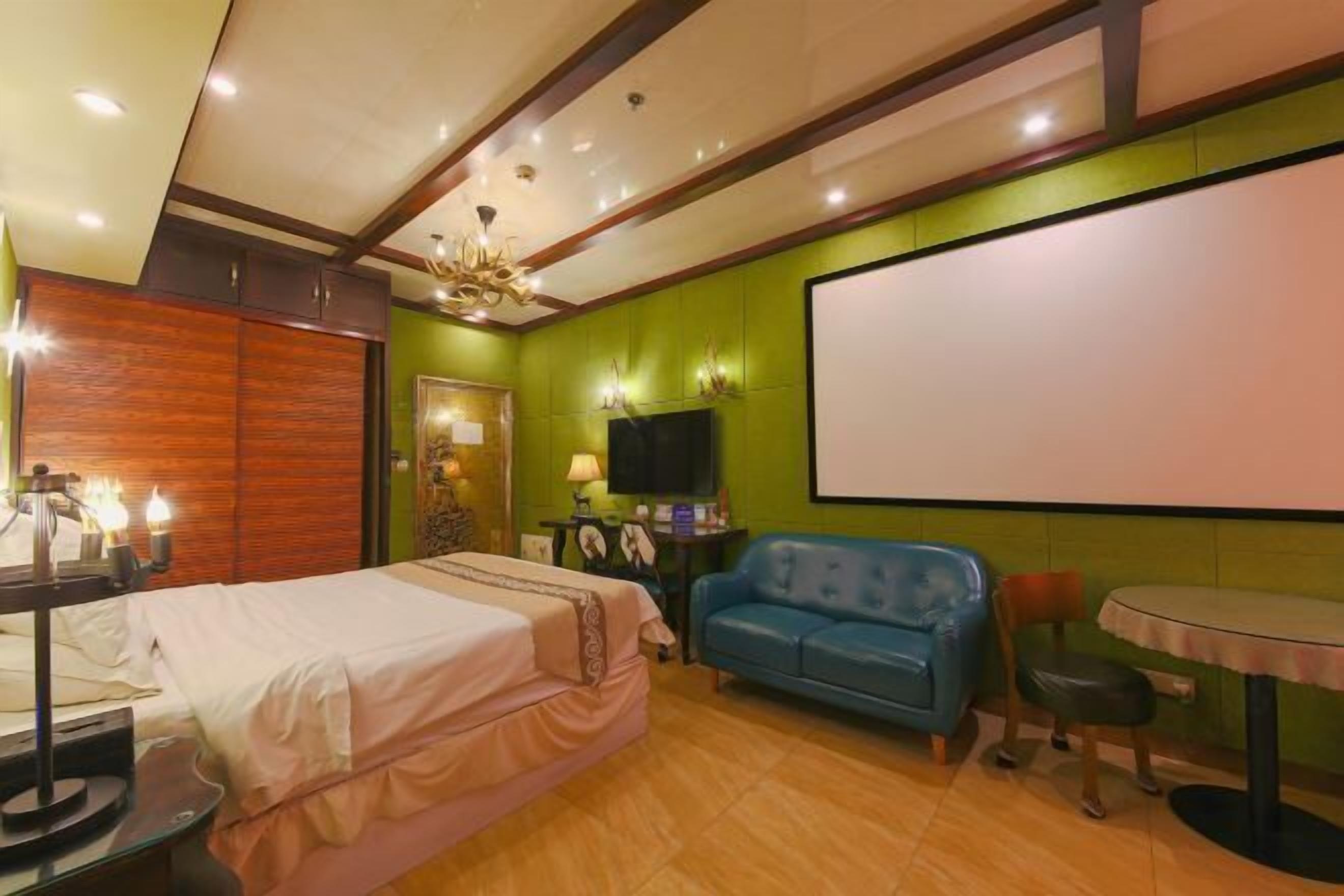 Een hotelkamer met een bed, een blauwe bank, een tafeltje, een televisie en een projectiescherm.