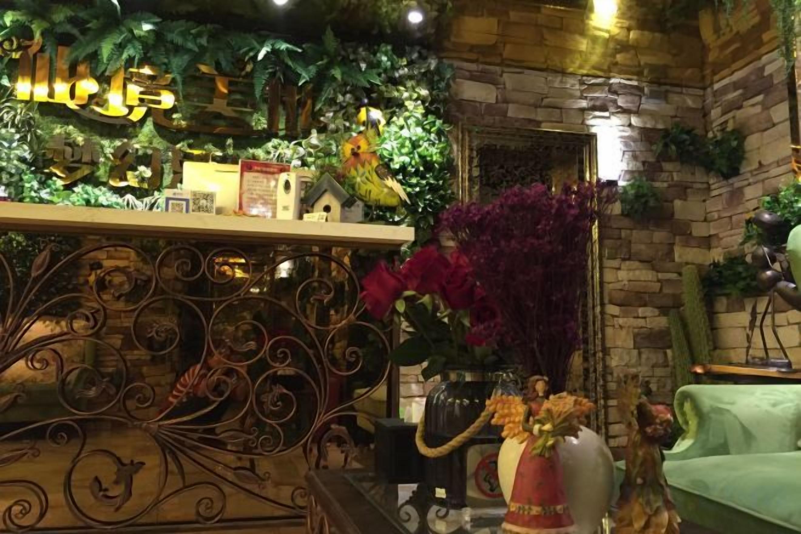 Una habitación con pared de ladrillo, un sofá verde, una barandilla decorativa de metal y una variedad de plantas y flores.