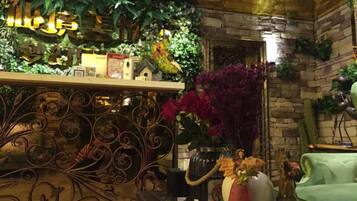 Una habitación con pared de ladrillo, un sofá verde, una barandilla decorativa de metal y una variedad de plantas y flores.