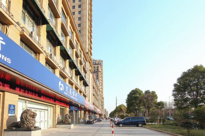 Un edificio de varios pisos con un toldo azul, estacionamiento y cielo despejado.