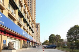 Un edificio de varios pisos con un toldo azul, estacionamiento y cielo despejado.