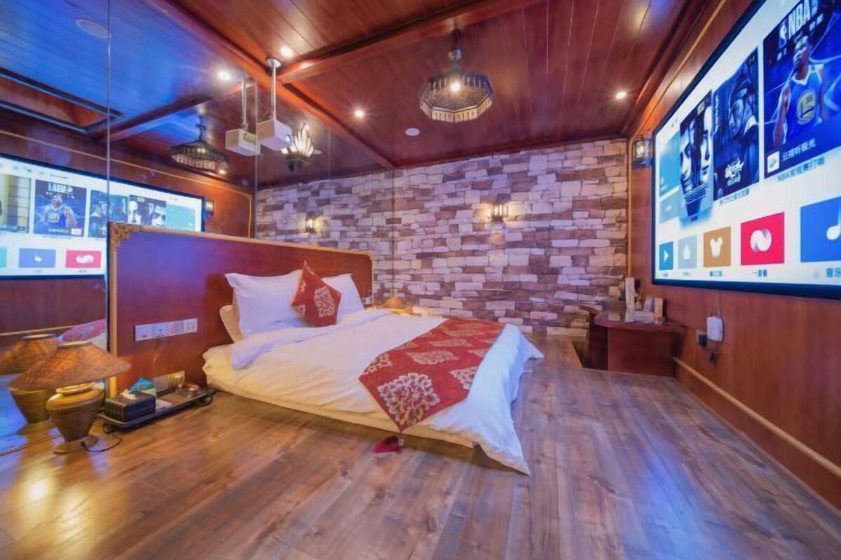 A modern hotel room with a brick wall, wooden ceiling, and a large bed with a red throw blanket.