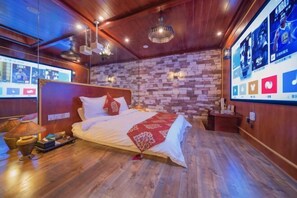 Une chambre d’hôtel moderne avec un mur en briques, un plafond en bois et un grand lit recouvert d’un plaid rouge.