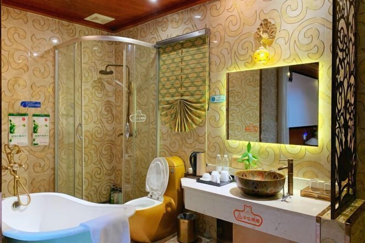 Une salle de bain équipée d’une baignoire, de toilettes et d’un espace douche. On y trouve un lavabo avec un miroir au-dessus, ainsi qu’un bol décoratif posé sur le comptoir.