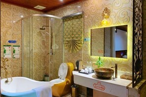 Une salle de bain équipée d’une baignoire, de toilettes et d’un espace douche. On y trouve un lavabo avec un miroir au-dessus, ainsi qu’un bol décoratif posé sur le comptoir.