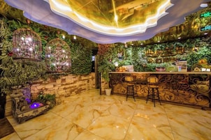 Una zona de bar con pared de piedra, follaje verde y suelo de mármol.