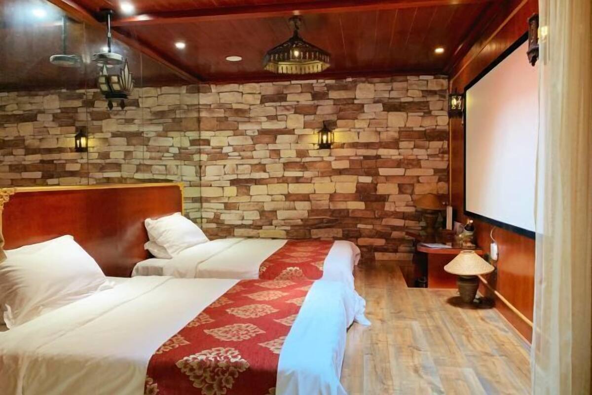 A hotel room with two beds, stone walls, wooden ceiling, and a projector screen.