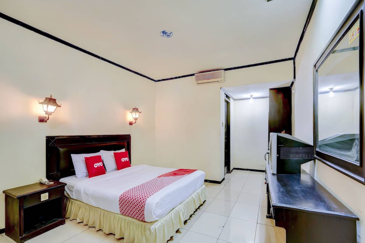 A hotel room with a bed, bedside table, lamp, and a large mirror.