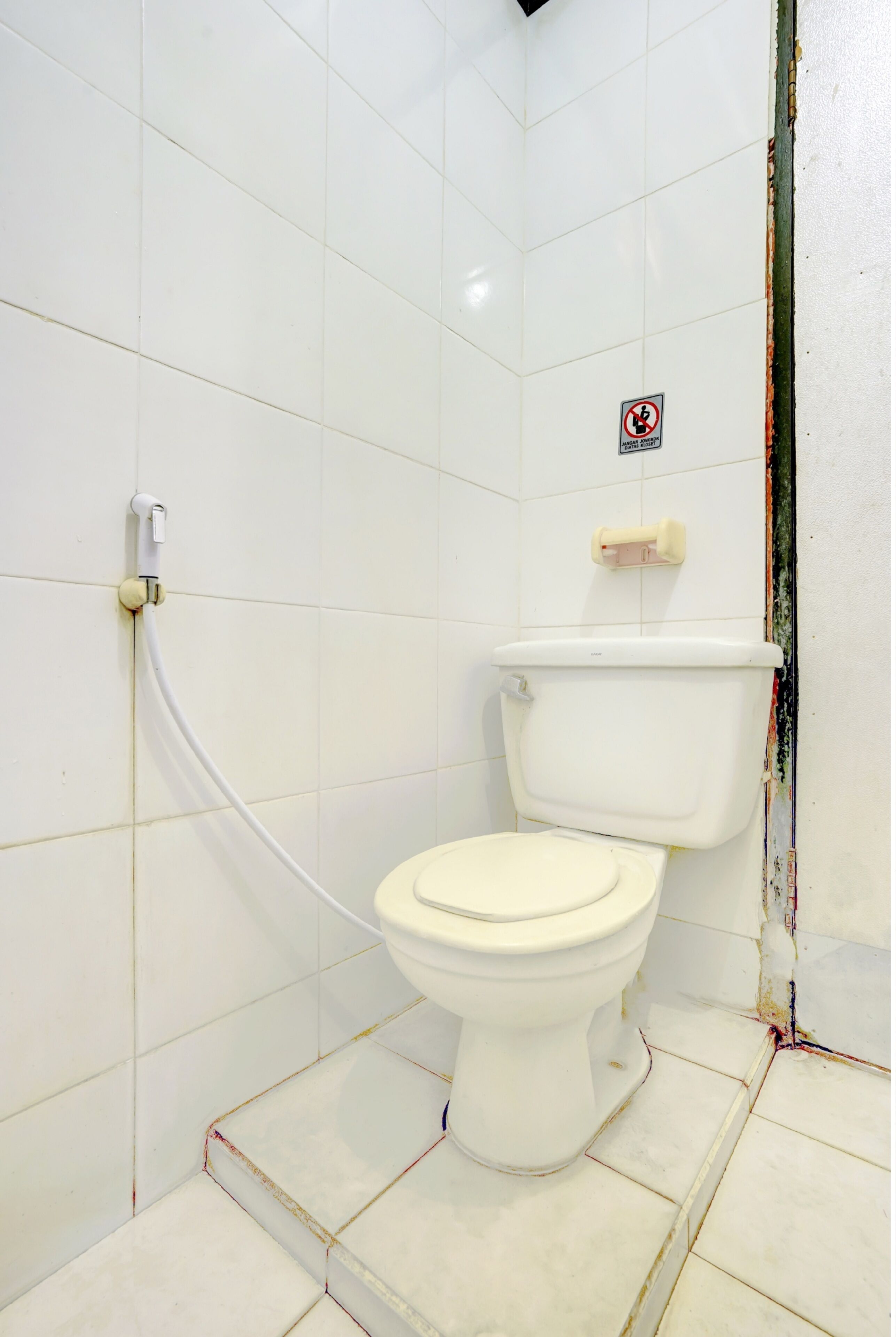 A small, white-tiled bathroom with a toilet, a hand dryer, and a no-smoking sign.