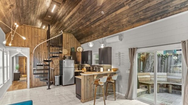 Una cocina moderna con techo de madera, una isla integrada con taburetes altos y un amplio ventanal corredera que da a un espacio exterior.
