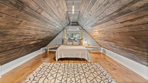 Una habitación con paredes de madera y techo inclinado, una cama con alfombra estampada, y una ventana con vistas.