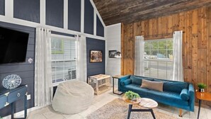 Una sala de estar con un sofá azul, un sillón inflable blanco y un televisor sobre una pared oscura.