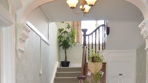 A grand staircase with a wooden handrail, a potted plant at the top, and a carpeted floor with a decorative pattern.